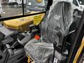 A new 2024 Caterpillar 306 excavator seat covered in plastic wrap with control levers and safety labels visible