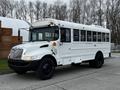 A white 2013 International 4200 bus with large windows and a high roof parked on a street with black tires and orange lights on top