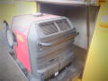 A red and black generator is positioned inside a vehicle with a handle for easy access and ventilation grills on the front