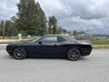 A black 2017 Dodge Challenger is parked on a paved surface showcasing its sleek design and sporty profile with distinctive wheels and a muscular stance