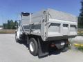 A 2005 Freightliner M2 106 Medium Duty truck with a grey dump bed and large rear wheels parked on a gravel surface