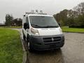 A 2018 RAM Promaster van with a white exterior parked on a wet surface featuring roof-mounted equipment and a black front grille