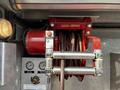 Red hose reel with a 100-foot hose coiled inside a metal frame mounted on a wall with control switches and pressure gauges below it