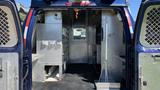 Interior view of a 2013 Ford Econoline with metal cabinets and shelving on both sides showing an organized workspace