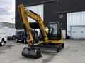 A yellow 2024 Caterpillar 306 compact excavator with a black bucket and a cabin for the operator in the foreground