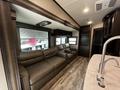 Interior of a 2021 Grand Design Recreational 311BHS featuring two brown leather sofas in a living area with overhead cabinets and a kitchen counter to the side