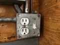 A metallic electrical outlet box with two outlets and a switch mounted on a wooden surface