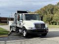 A 2012 International 4300 truck with a white and silver body and a flatbed design parked on a street