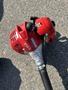 A red Shindaiwa gas powered weed eater with a metal shaft and a curved head attachment lying on a flat surface
