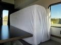 A 2017 Ford Transit interior with two large white mattresses neatly arranged against the wall next to a dark wooden table