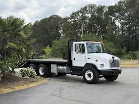 A white 1998 Freightliner FL80 flatbed truck with black accents and a visible chassis parked on a paved area