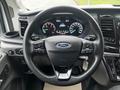 The interior of a 2021 Ford Transit featuring a black steering wheel with control buttons and a Ford emblem in the center