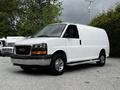 A white 2023 GMC Savana van with a chrome grille and wheels is parked on a gravel surface