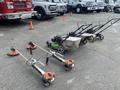 Three Honda Lawnboy mowers and two Stihl line trimmers positioned on the ground with their handles upright and engines visible