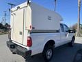 A white 2016 Ford F-250 SD with a cargo box on the back and a camper shell is parked on a road