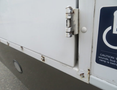 Close-up of a hinge on the side door of a 2020 Chevrolet Express with visible rust and a handicap sign nearby