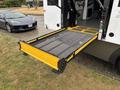 A lowered wheelchair lift from the back of a 2020 Chevrolet Express van with a metal mesh surface and yellow trim