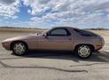 A 1983 Porsche 928 in a muted color with a sleek design featuring a long hood and sloping rear roofline