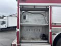 A 2006 E-One Typhoon fire truck with an open storage compartment revealing metal shelving and tools inside