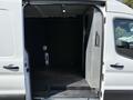 A 2022 Ford Transit van with an open rear door revealing a spacious cargo area featuring a flat floor and minimal interior fittings