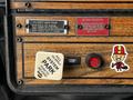 A control panel featuring labeled switches and a large white lever for the main pump with a parking brake button and a playful sticker of a cartoon character in a top hat