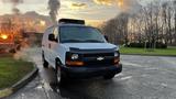 A white 2005 Chevrolet Express van with a black grille and chrome details parked on a street with a sunset in the background