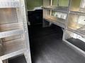 Empty interior of a 2023 Ford Transit van featuring metal shelving units on both sides and a black floor with no other items present
