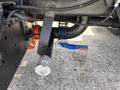 A close-up of a 2015 Ford F-750's undercarriage showing a black pipe connected to a valve with a blue handle and a metal cap attached with a chain