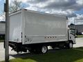 A 2016 Isuzu NQR box truck with a white cargo area and a black chassis parked on the side of the road