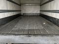 A 2018 Isuzu NRR truck with an empty cargo area featuring a flat, textured floor made of wood with metal strips along the sides