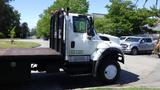 A 2015 International 7400 truck in white with a flatbed and a black grill visible from the side angle