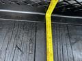 A measuring tape laid flat on a textured surface adjacent to a black truck bed, indicating measurements for a 2016 Ford F-550