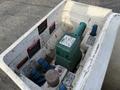 A green hydraulic pump with control levers and buttons is placed in a white container with warning labels attached