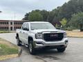 A white 2016 GMC Sierra 1500 pickup truck parked on a street with a chrome grille and large tires