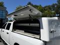 A white 2016 RAM 2500 pickup truck with a raised camper shell and an open rear cover displaying storage space inside