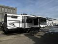 A 2021 Grand Design Recreational 311BHS camper with a sleek black and white design featuring an awning extended on one side and two axles visible underneath