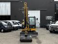 A 2024 Caterpillar 306 excavator positioned facing forward with a large bucket attachment at the front and a glass-enclosed cabin for the operator