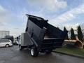 A 2015 Isuzu NPR HD dump truck with its bed raised, showing the unloading mechanism in action