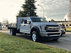 A silver 2018 Ford F-450 Super Duty truck with a flatbed and a tool box mounted on the rear