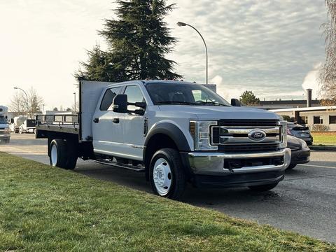 A silver 2018 Ford F-450 Super Duty truck with a flatbed and a tool box mounted on the rear