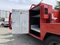 A 2013 Ford F-550 with an open storage compartment showing shelves inside and a red exterior with a fire extinguisher mounted on the side