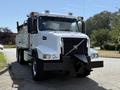 A 2005 Volvo VND truck in white with a black grill and plow attachment at the front featuring dual headlights and a dump bed in the rear