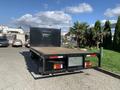 A 2015 Isuzu NPR flatbed truck with a wooden deck and a tall black rear wall positioned in a parking area