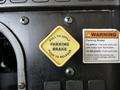 A yellow diamond-shaped parking brake control labeled "PULL TO APPLY" and "PUSH TO RELEASE" next to a warning sign for proper usage and safety instructions