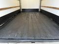 A clean and empty truck bed interior of a 2016 Isuzu NQR with a polished wooden floor and black rubber lining along the sides