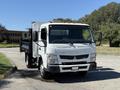 A 2015 Mitsubishi Fuso FE truck with a flatbed and a silver cargo box attached, featuring a white cab and multiple roof lights