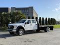 A white 2020 Ford F-550 with a flatbed design parked with a row of tall, greenery-lined hedges in the truck bed