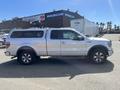 A 2014 Ford F-150 in silver with a truck bed cover and chrome wheels seen from the side