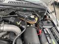 Engine compartment of a 2003 Ford F-450 SD showing components like air intake pipes cooling system tank and battery with various electrical connections and labels