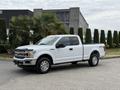 A white 2018 Ford F-150 truck with a black hood and chrome grille positioned in a forward angle on a paved surface